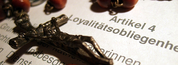 Kreuz und Rosenkranz, auf dem Text des Artikels 4 über die Loyalitätsobliegenheiten für eine Anstellung in der katholischen Kirche liegend 